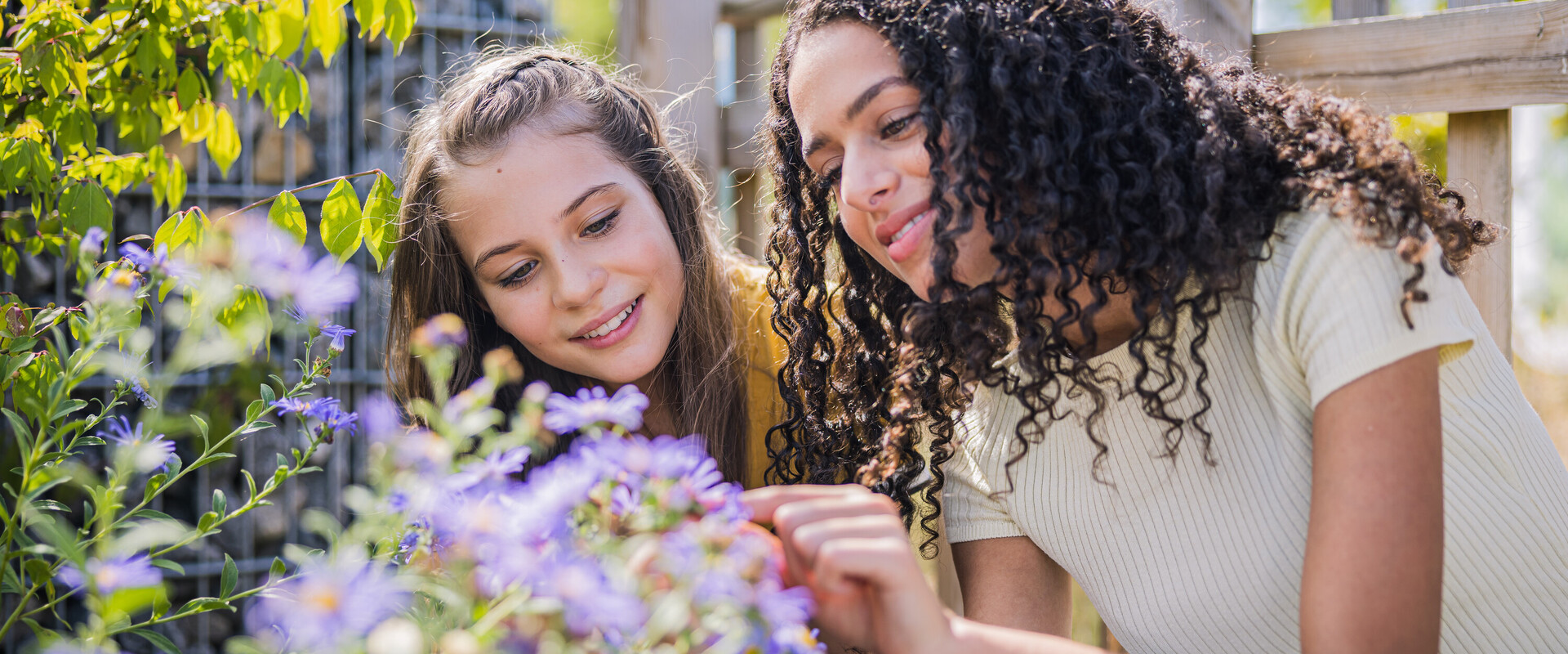 Zwei M&auml;dchen sitzen vor einer Pflanze und betrachten die Bl&uuml;ten.